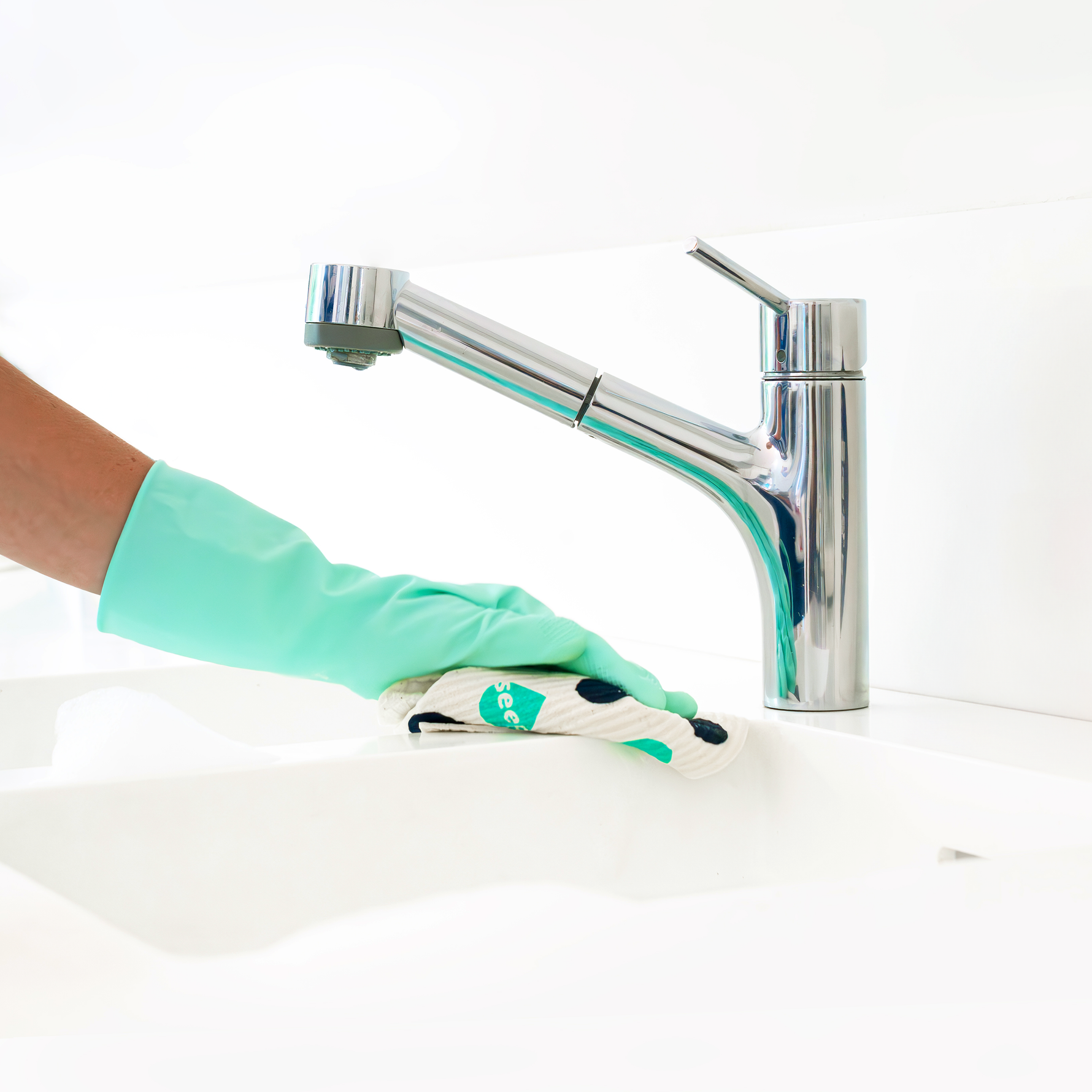 Turquoise rubber gloves on hand using Seep Eco Sponge Cloth to wipe white sink