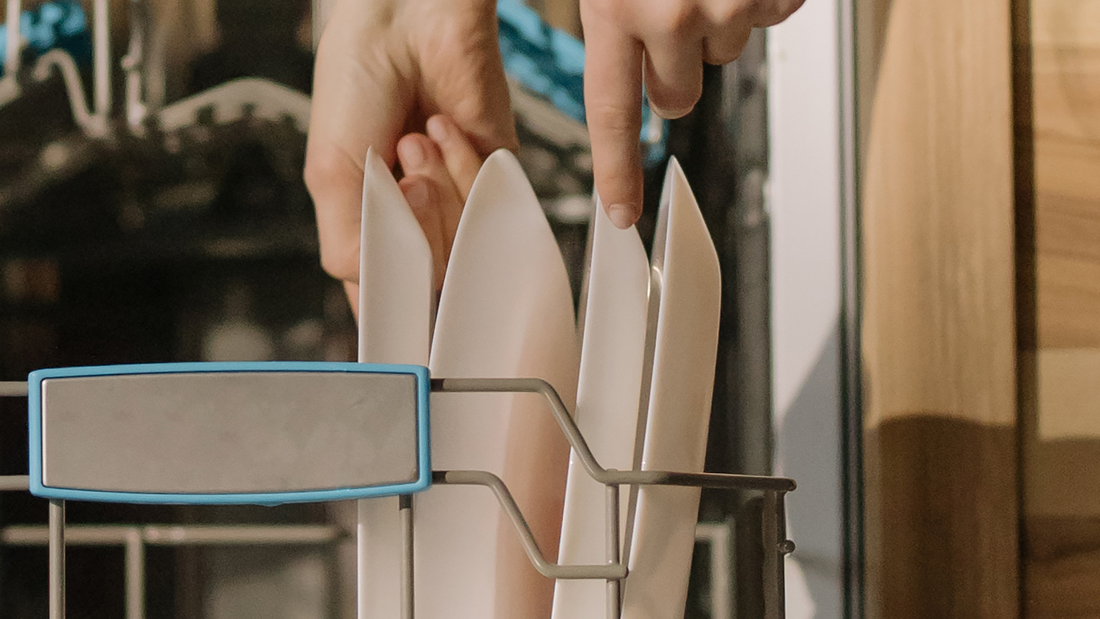 Hands putting white plates in dishwasher