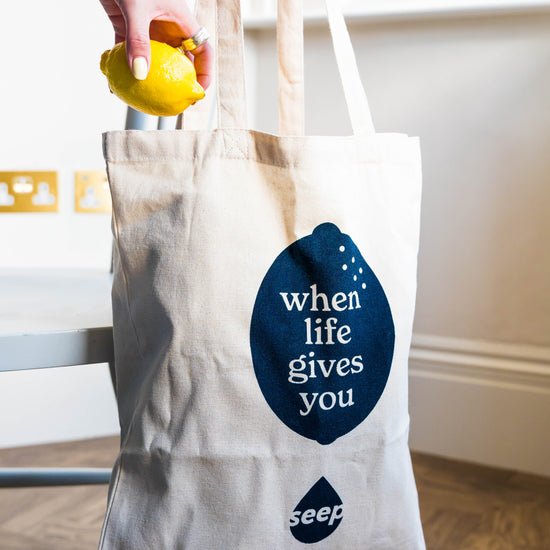 Branded tote bag with slogan "when life gives you" inside a navy lemon shape