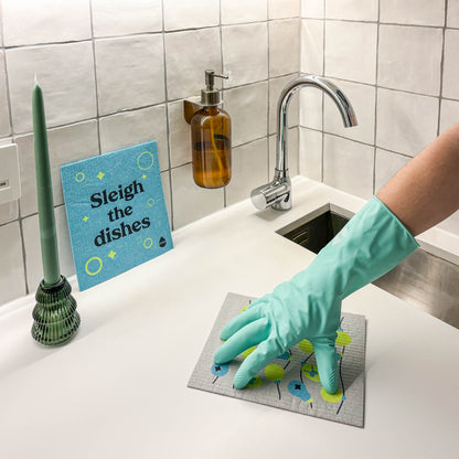 Hand wearing rubber gloves wiping kitchen countertop with festive sponge cloth