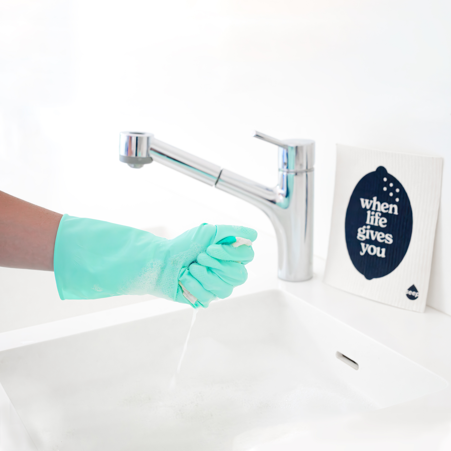 Hand with rubber gloves squeezing water out of sponge cloth