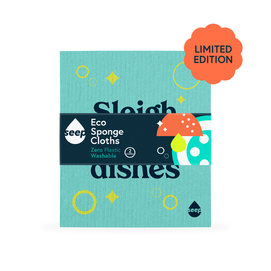 A plastic-free sponge cloth with bubbles, pings and "Sleigh the dishes" slogan printed on it, with a recyclable label around it