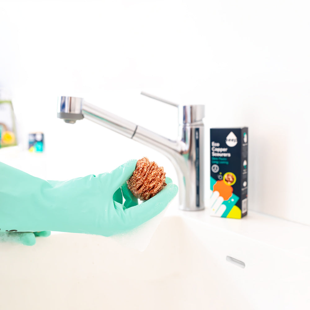 Hand in Eco Rubber Gloves holding Recyclable Copper Scourer above kitchen sink